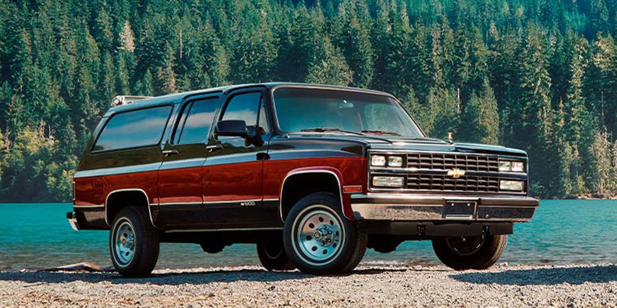 Chevrolet Suburban clásica estacionada frente a un lago y un bosque.